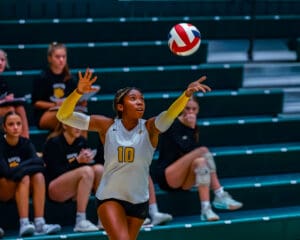 Female volleyball player serving in a match, intense focus, teammates watching in the background.