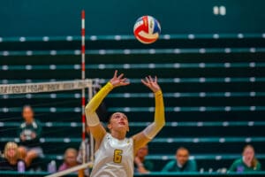 Volleyball player in yellow sets the ball during a match in a gymnasium.