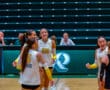 Volleyball team players celebrating a point during a match on an indoor court.