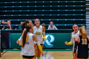 Volleyball team players celebrating a point during a match on an indoor court.