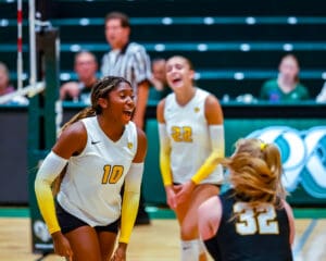 Women's volleyball players celebrate point during a match, wearing white jerseys with numbers 10 and 22.