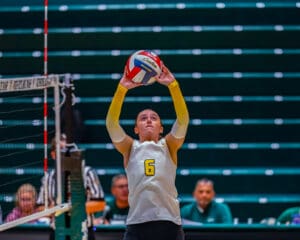 Volleyball player number 6 sets the ball during a match indoors, wearing a yellow and white uniform.