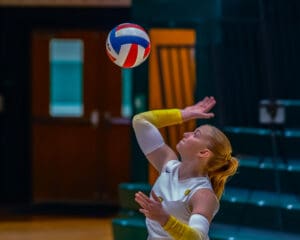 Volleyball player preparing to serve during a match, wearing a white and yellow uniform, indoors.