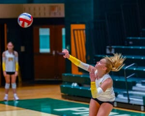 Volleyball player serves ball during intense match on indoor court.