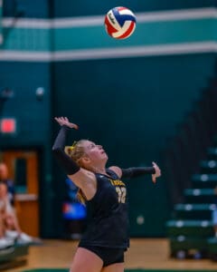 Volleyball player executing a powerful jump serve during a match in a gymnasium.
