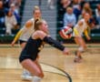 Volleyball player diving to pass the ball during a competitive indoor match, with teammates in the background.