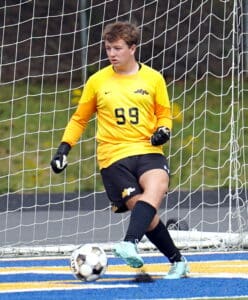 Soccer goalie in yellow jersey kicks ball, guarding the net during outdoor game on colorful field.