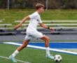 Soccer player in white uniform dribbles the ball on a green field during a match.