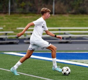 Soccer player in white uniform dribbles the ball on a green field during a match.