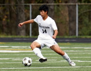 Soccer player in white jersey dribbling on green field, focused and determined in action.