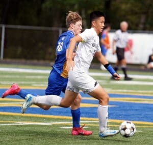 Two soccer players compete for the ball on a field during a match, one in white and the other in blue.