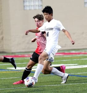 Two soccer players compete for the ball during an intense match on a green field, showcasing athletic skill.