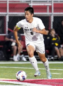 Soccer player in action, dribbling ball on field during a match, wearing North Allegheny uniform.