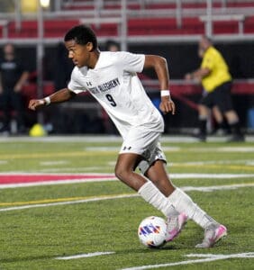 Soccer player in white uniform dribbling on a field during a night match.