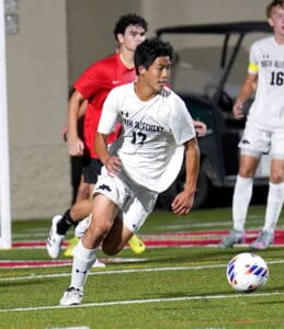 Soccer player in white sprinting towards the ball during a match on a field, with teammates and opponents nearby.