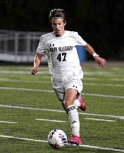 Soccer player in white jersey sprinting on field, focused on dribbling the ball during a competitive night match.