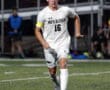 Soccer player from North Allegheny in action on a field at night, wearing white jersey and dribbling a ball.