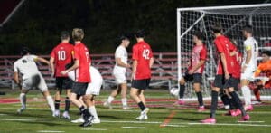 Soccer players mid-game near the goal, team in red defends against team in white during a nighttime match.
