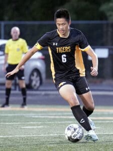 Soccer player in black and yellow uniform dribbles ball during a match on a field.