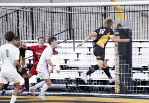 Soccer player jumping to score a goal during an intense match, with goalie and defenders in action.