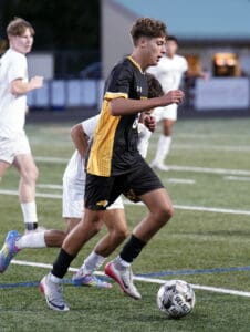 Soccer player in black and yellow uniform dribbling the ball on a field during a match.