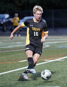 Soccer player in black and yellow Tigers uniform dribbling the ball on the field during a game.