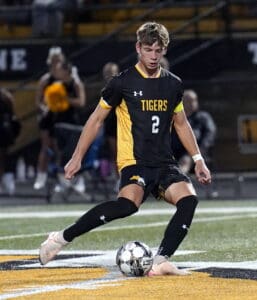 Soccer player in black and yellow striped uniform controlling the ball on a field during a game.