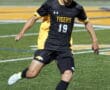 Soccer player dribbling the ball on a turf field in a game, wearing a black jersey with number 19 for the Tigers.