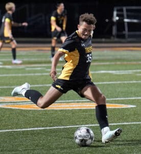 Soccer player in yellow and black uniform kicking ball on field during a night match.