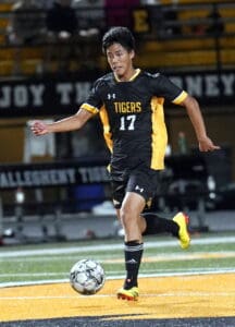 Soccer player in black and yellow jersey dribbling a ball on the field at night, focused on the game.
