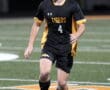 Soccer player in black Tigers jersey dribbles ball on field during night game.