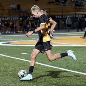 Soccer player in black and yellow uniform dribbling ball on field at night game.