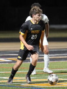 Soccer player in black and yellow Tigers uniform controlling the ball during a match on a lit field.