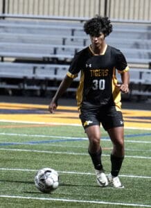Soccer player in black and yellow uniform dribbling ball on field during nighttime match.