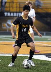 Soccer player in black jersey controlling ball on field during match.