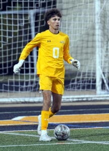Soccer goalie in yellow uniform prepares to kick the ball during a match on a turf field.