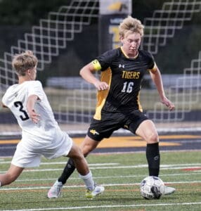 Soccer player in black jersey dribbling past a defender in white on a field during a competitive match.