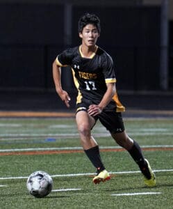 Soccer player in black and yellow uniform dribbles ball on field during night game.