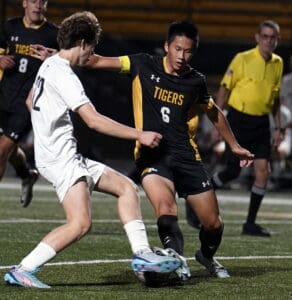 Soccer players compete for the ball during a night match, with referee observing action on the field.