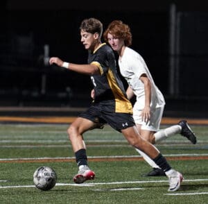 Soccer players in action during a night match, one dribbling the ball, both in contrasting black and white uniforms.