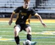 Soccer player in black and yellow jersey dribbles ball on field during match; athletic action shot.