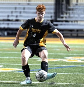 Soccer player in black and yellow jersey dribbles ball on field during match; athletic action shot.