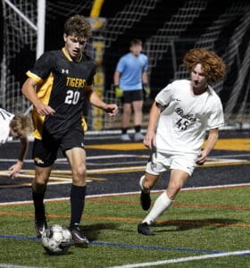 Soccer players in action on the field during a match at night, with focus on the player in the black jersey.