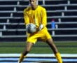 Soccer goalie in yellow uniform catching a ball during a game on a nighttime field.