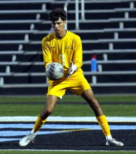 Soccer goalie in yellow uniform catching a ball during a game on a nighttime field.
