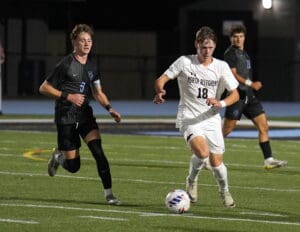 Soccer player in white jersey advancing the ball past opponent in black on a field during a night match.