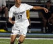 Soccer player in white kit dribbling the ball on a field during a night match.