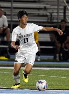 Soccer player in white kit dribbling the ball on a field during a night match.