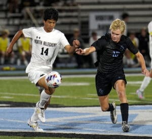 Two soccer players from opposing teams competing fiercely for the ball on a field.