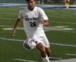 Soccer player in white uniform focused on controlling the ball during a game on a field at night.